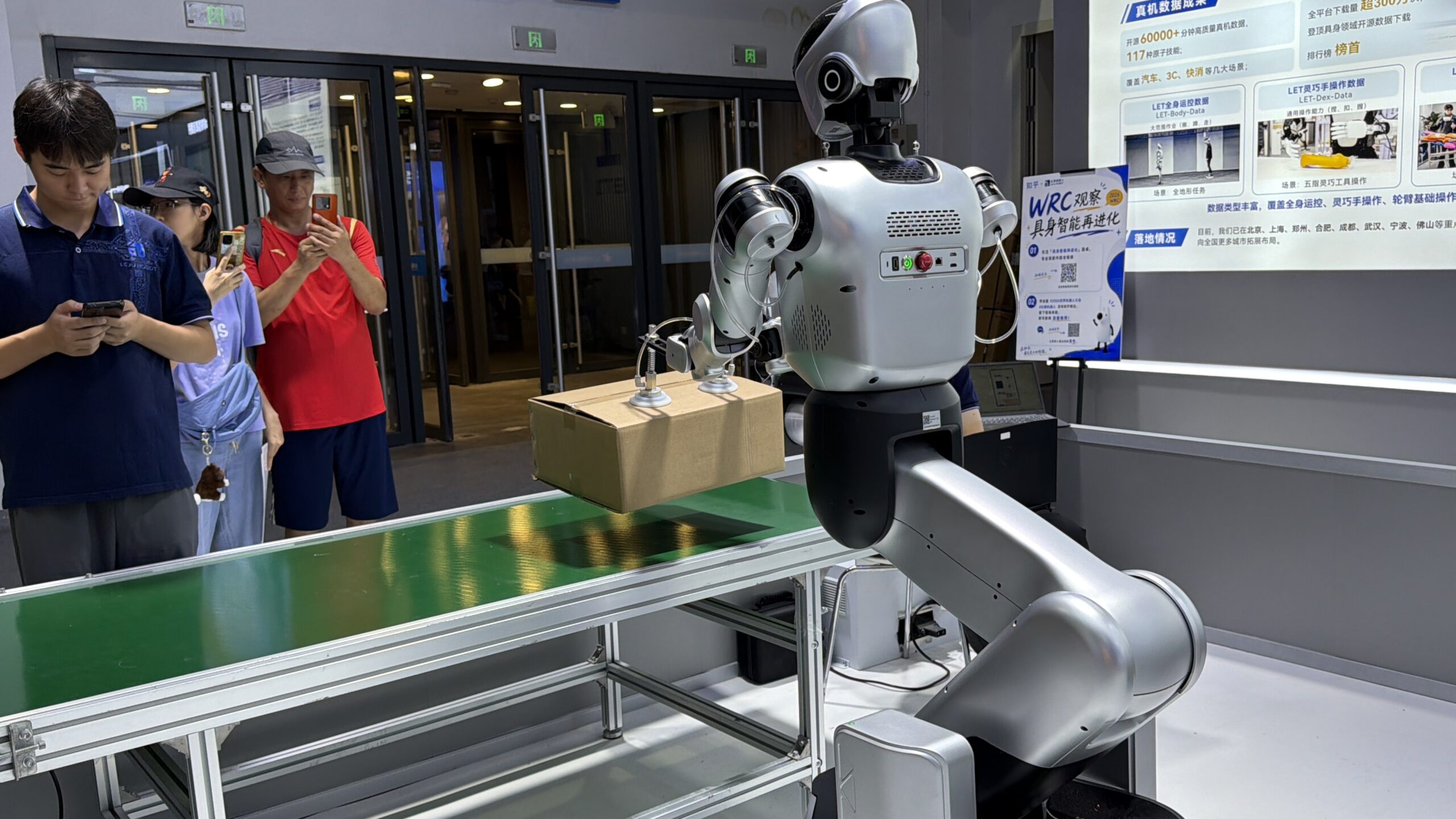 北京WRC2026で、箱を持ち上げるロボットの実機デモを確認する様子